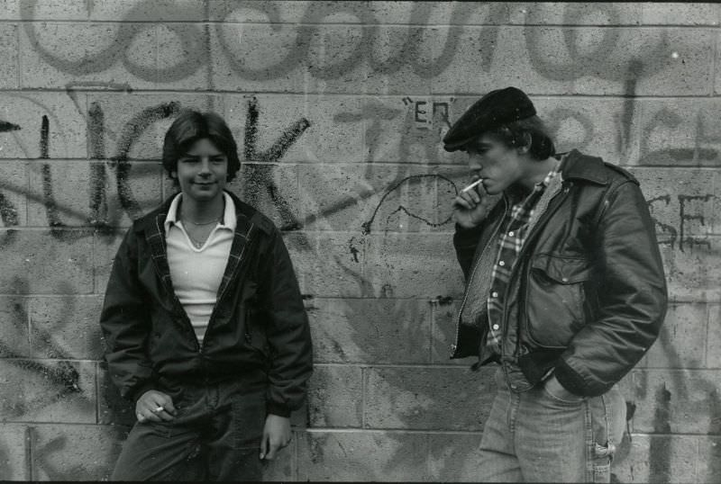 Two teenagers smoking against wall