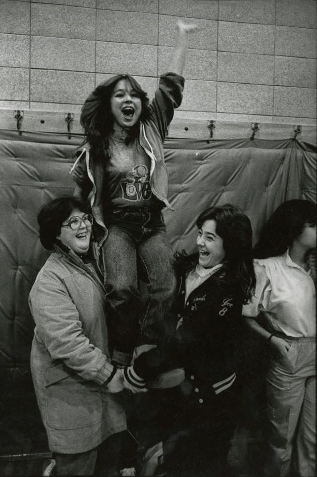 Two teenage girls hold up a third cheering teenage girl