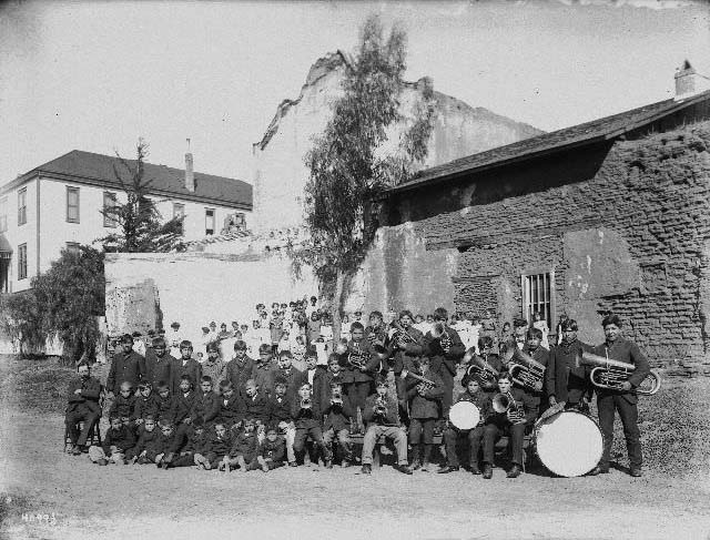 A Native American band standing near the Mission San Diego de Alcala, 1895