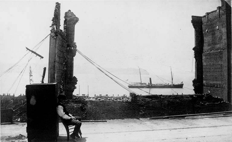 A man leaning up against a bank safe in the ruins of a building, 1889