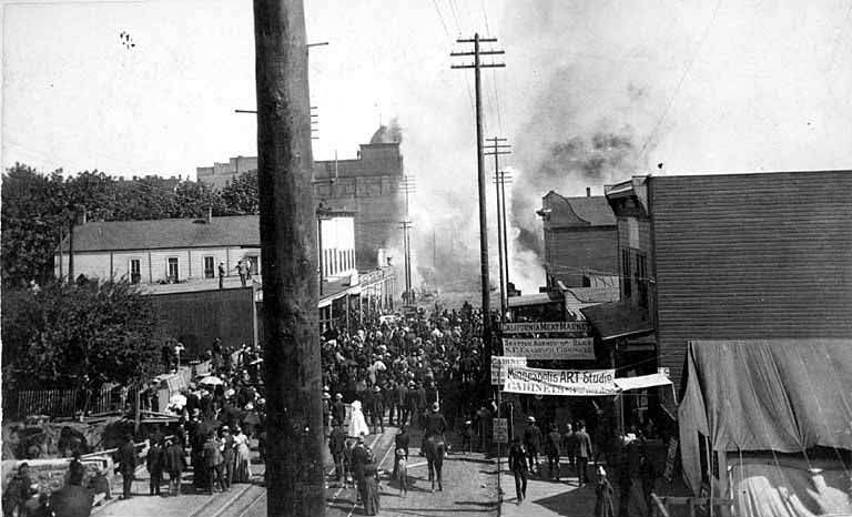 Frye's Opera House catching fire, with Minneapolis Art Studio on the right and a large crowd of people gathering in the street (recto), 1889