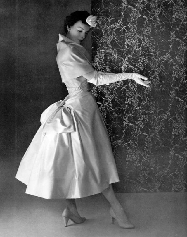 Victoria von Hagen in white satin dinner dress featuring bustle-like bow gathered in the back by Christian, 1953