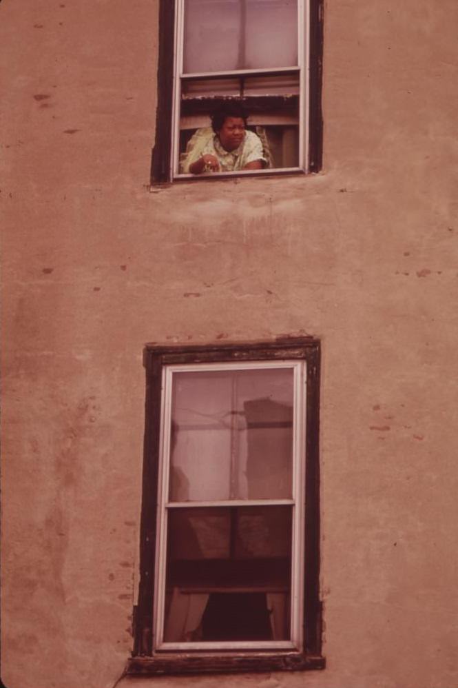 Woman Looks Out Of The Window Of Her Apartment In North Philadelphia, August 1973