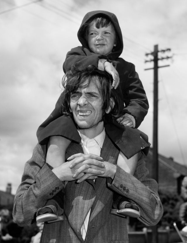 Father and son watching a parade, West End, Newcastle, UK, 1980