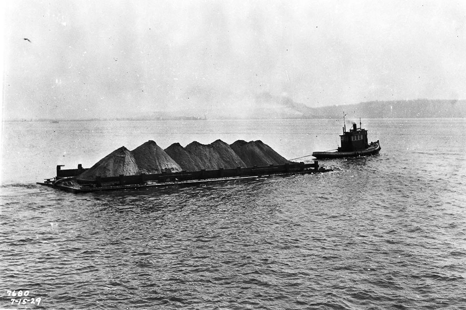 A tugboat tows a skow full of earth out into the harbor.