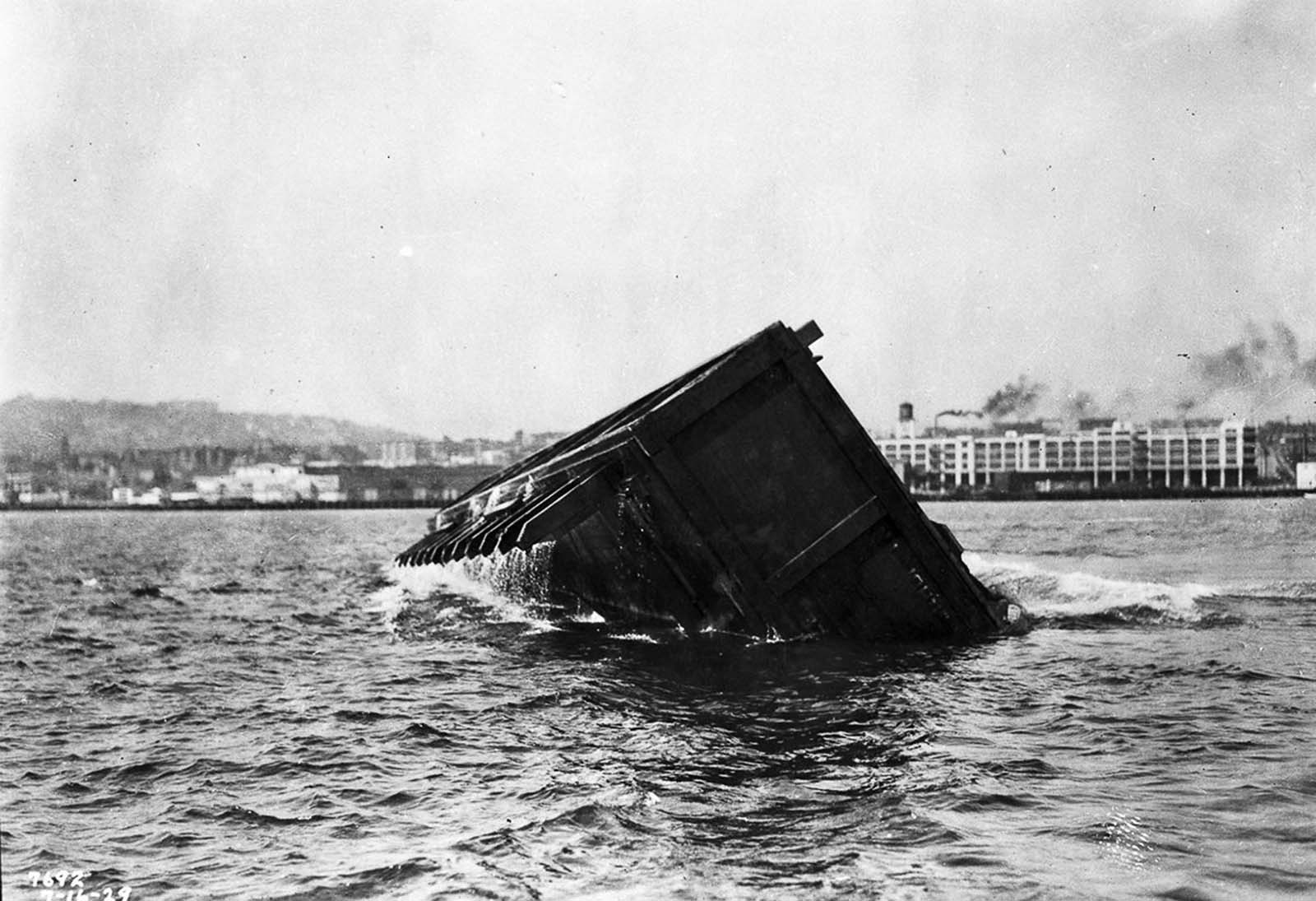 A self-capsizing scow carrying earth dumps its load into the city’s harbor.