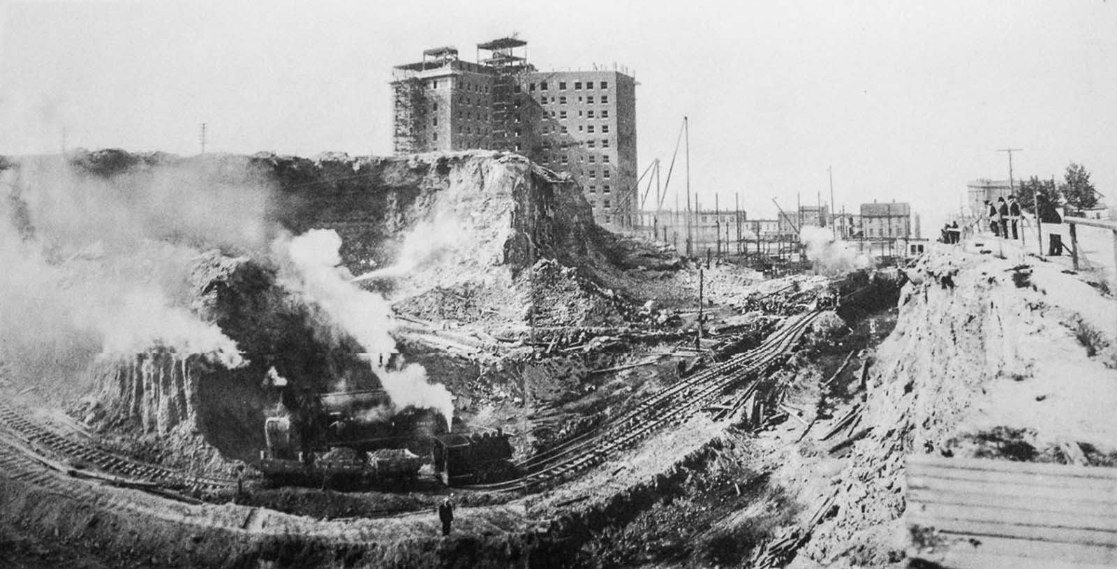 Trains move loose earth at the south summit of Denny Hill near the under-construction New Washington Hotel, at the corner of Second Avenue and Stewart Street.