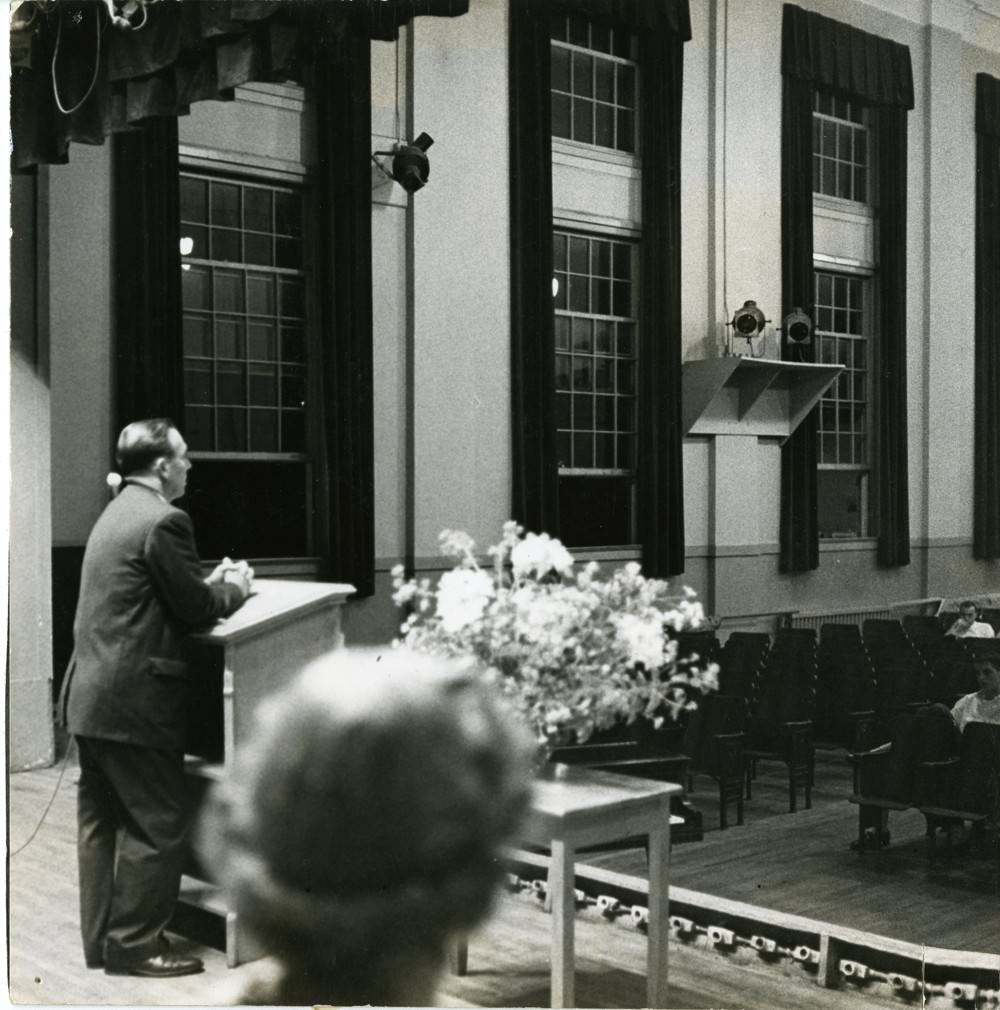 Inside old central high, with a unidentified man speaking on a stage, at a graduation ceremony, 1970s