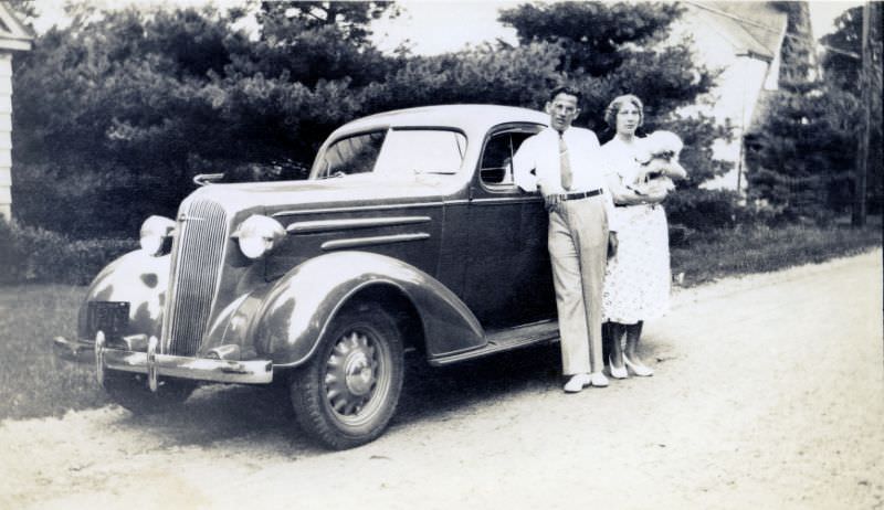 A stylish couple posing with a 1936 Chevrolet Standard Coupe on a gravel road in the countryside on July 22, 1936