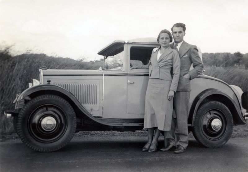 A stylish couple posing with a two-tone Peugeot 201 Cabriolet by the side of a country road, circa 1936