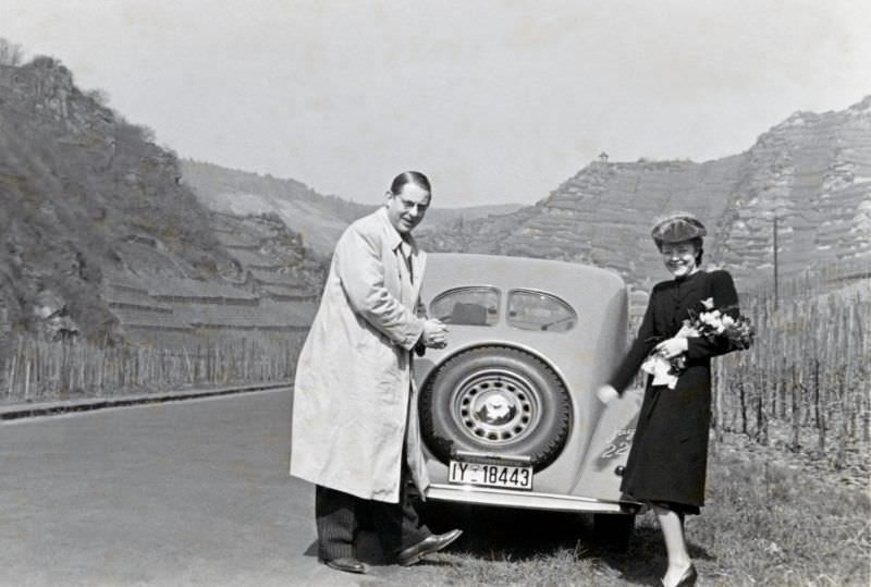 A cheerful couple posing with a Steyr 220 Limousine on a country road in the Ahr Valley, a wine-growing region south of the city of Bonn.