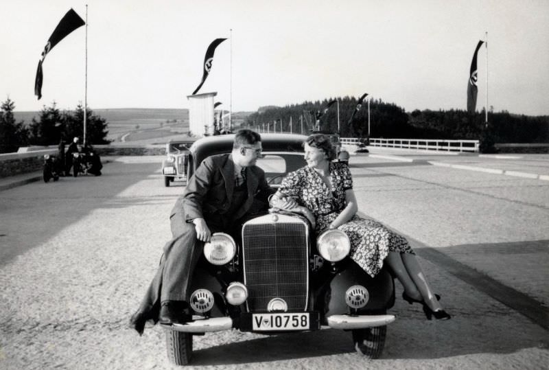 A fellow in a pinstripe suit and a lady in a floral dress posing on the fenders of a Mercedes-Benz 170 V, near the town of Plauen in Saxony.