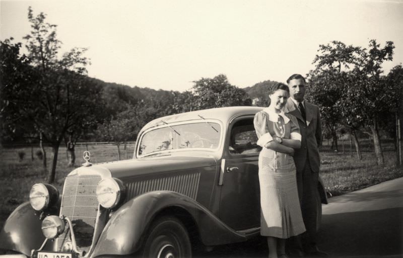 A lady in a short-sleeved dress and a fellow in a suit posing with a Mercedes-Benz 170 V in the countryside.