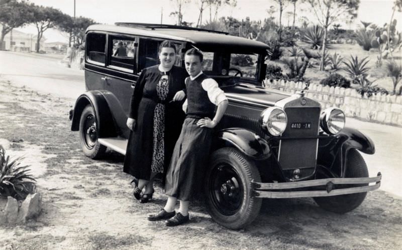 A young couple posing with a Fiat 521 Berlina on the side of a road lined with Italian stone pines.
