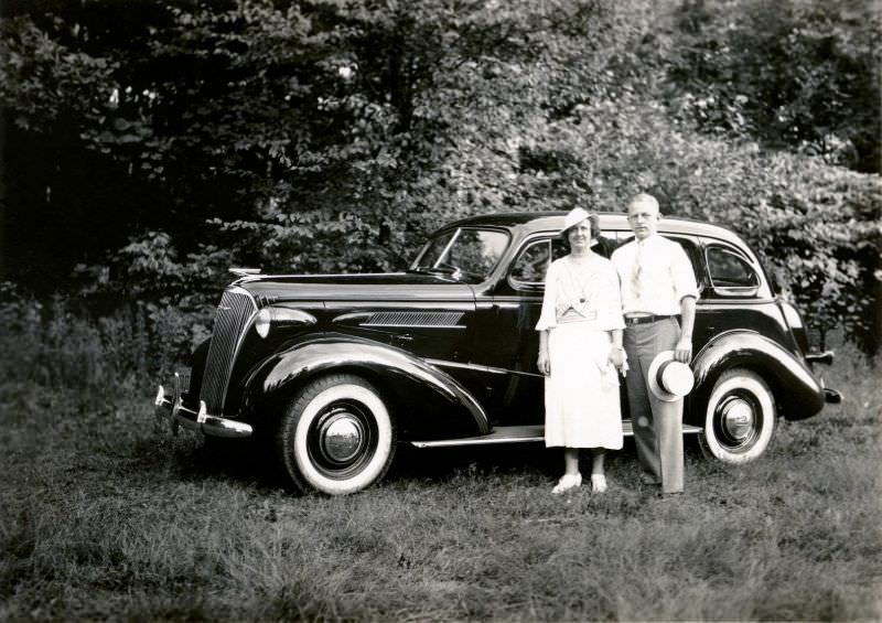 A middle-aged couple from Brooklyn posing with a shiny 1937 Chevrolet Master De Luxe in the countryside.