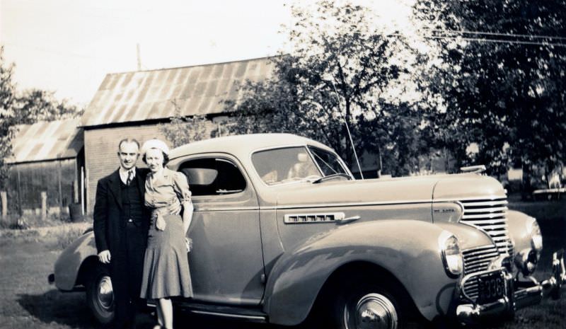 A middle-aged couple posing with a 1939 DeSoto Business Coupe in a back yard in summertime, 1939
