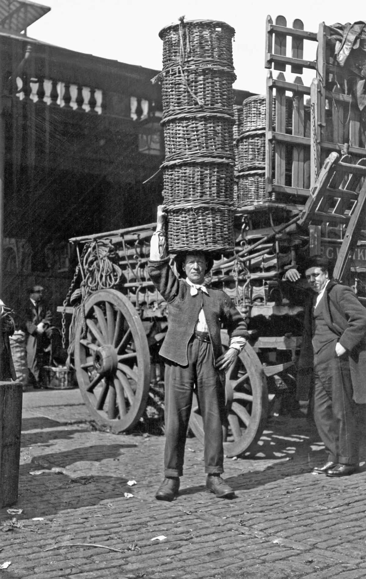 A market trader with a stack of baskets, 1915.