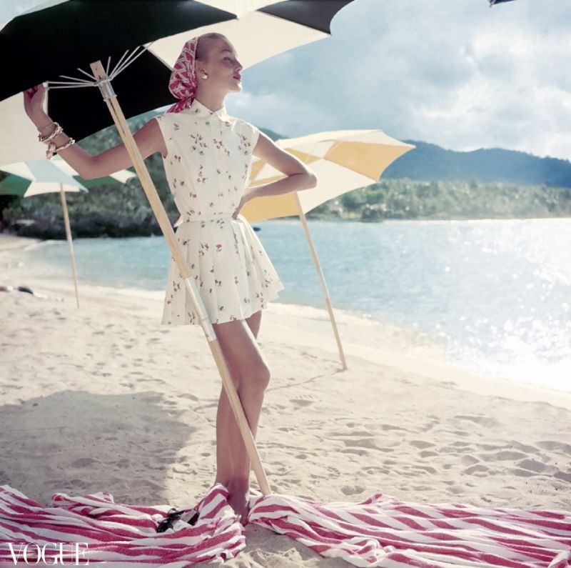 Model standing under beach umbrella wearing summer dress look; pleated short shorts and matching sleeveless shirt, both in a light floral pattern, Vogue, June 1954