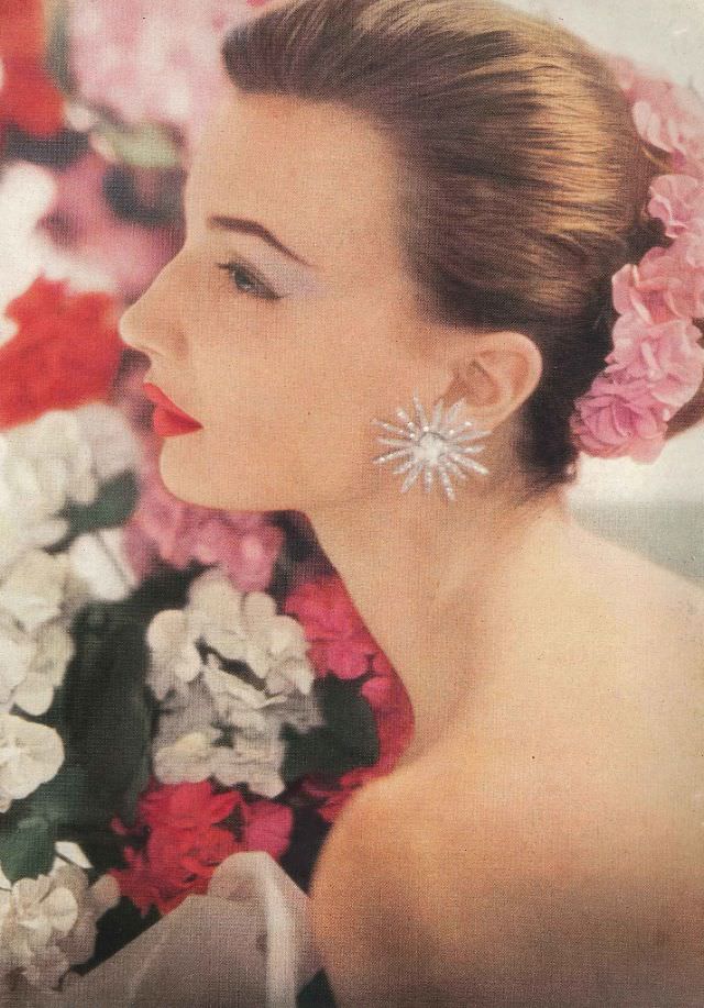 Maria Reachi wearing her hair swept back in a flowered-garlanded chignon. Her lipstick is 'Pink Geranium' by Charles of the Ritz, Vogue, June 1952