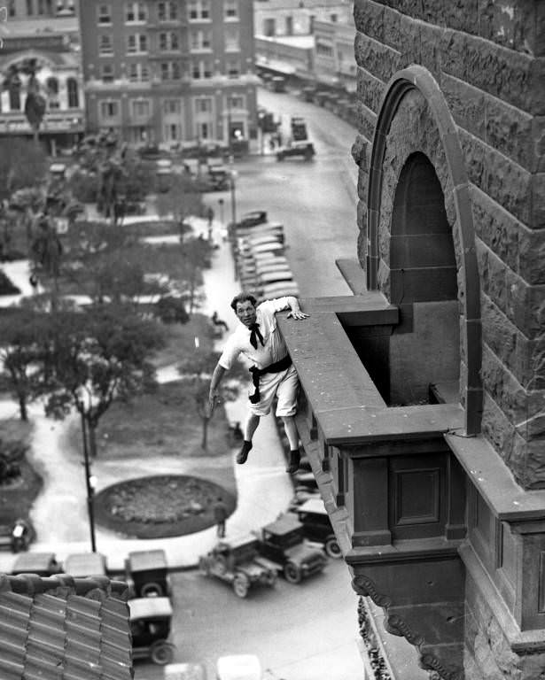 Human fly" Babe White hanging from balcony of the Bexar County Courthouse overlooking Main Plaza, 1925