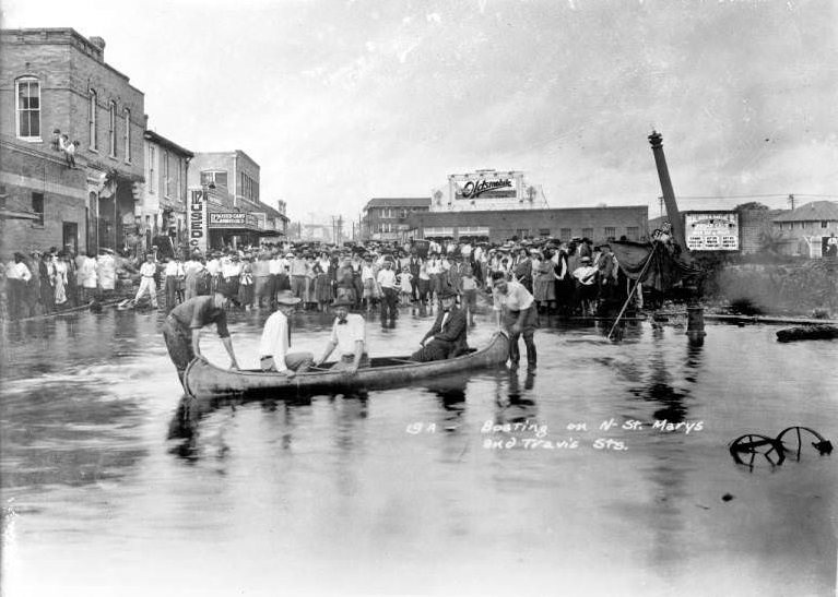 Crowd watching men in a canoe on the floodwaters of the San Antonio River at the intersection of St. Mary's and Travis Streets, 1921
