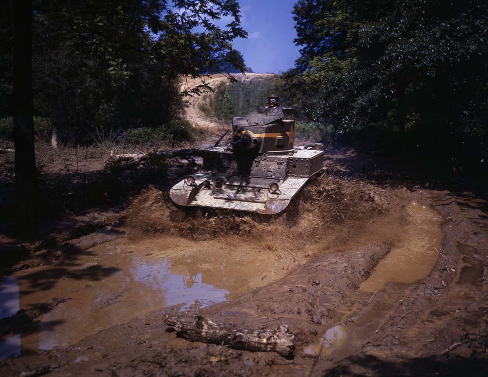 An M3 Stuart light tank drives through a water obstacle.
