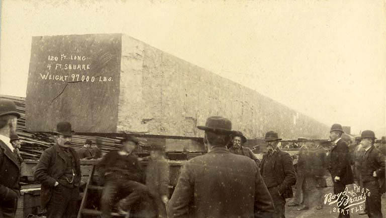 Men standing near railroad car loaded with large piece of timber for the Chicago World's Fair, 1893