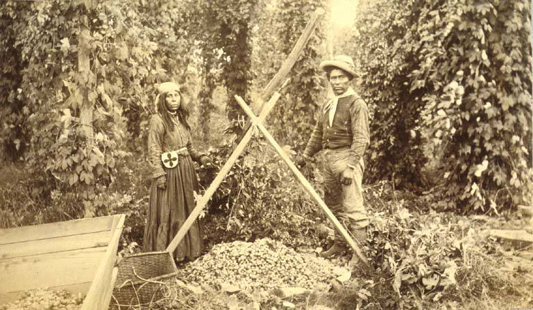 Two Puget Sound Indians, a man and a woman, standing in a hop field, unidentified farm, 1889