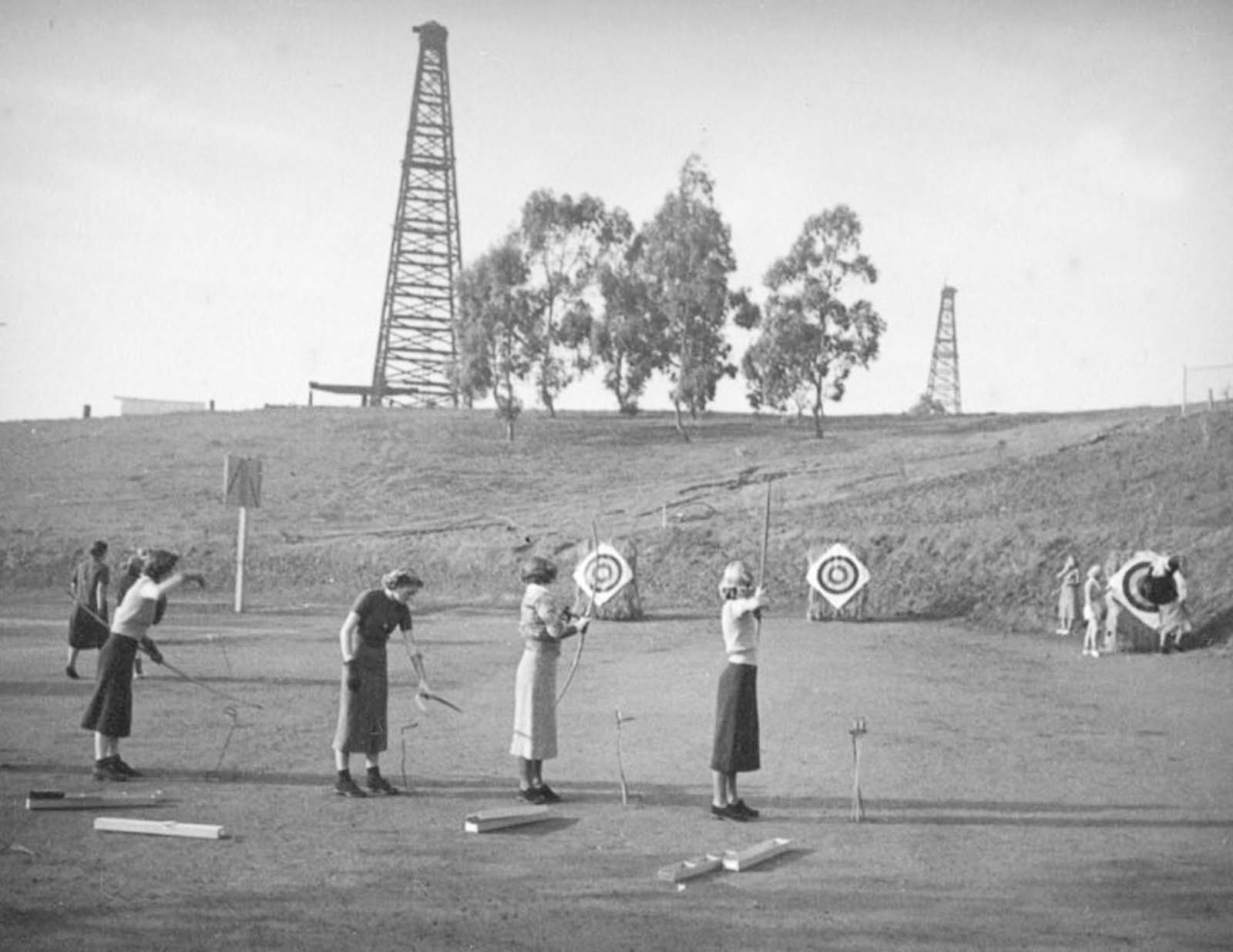 Students practice archery at Beverly Hills High School, with oil derricks nearby