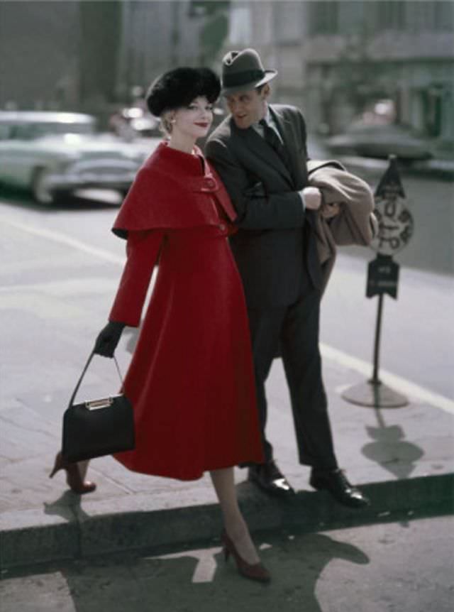 Model is wearing a crimson coat with a high waist buttoned-on cape by Young Couture, fox hat by Emme, 1956