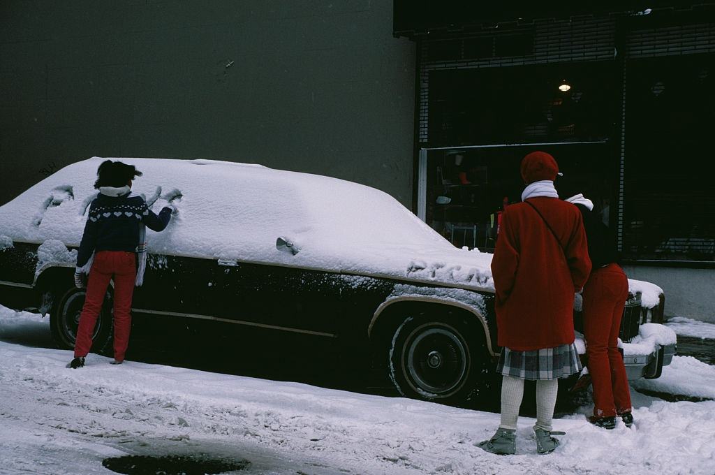 A girl writing in the snow covering a car in New York City, during the blizzard of January 1996.