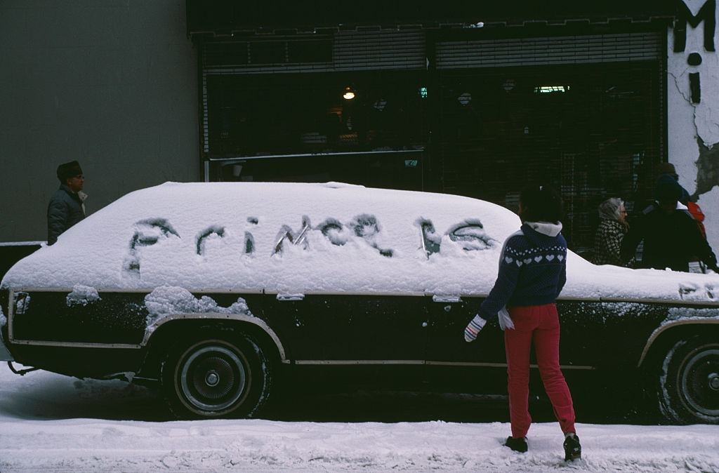 A girl writing in the snow covering a car in New York City, during the blizzard of January 1996.