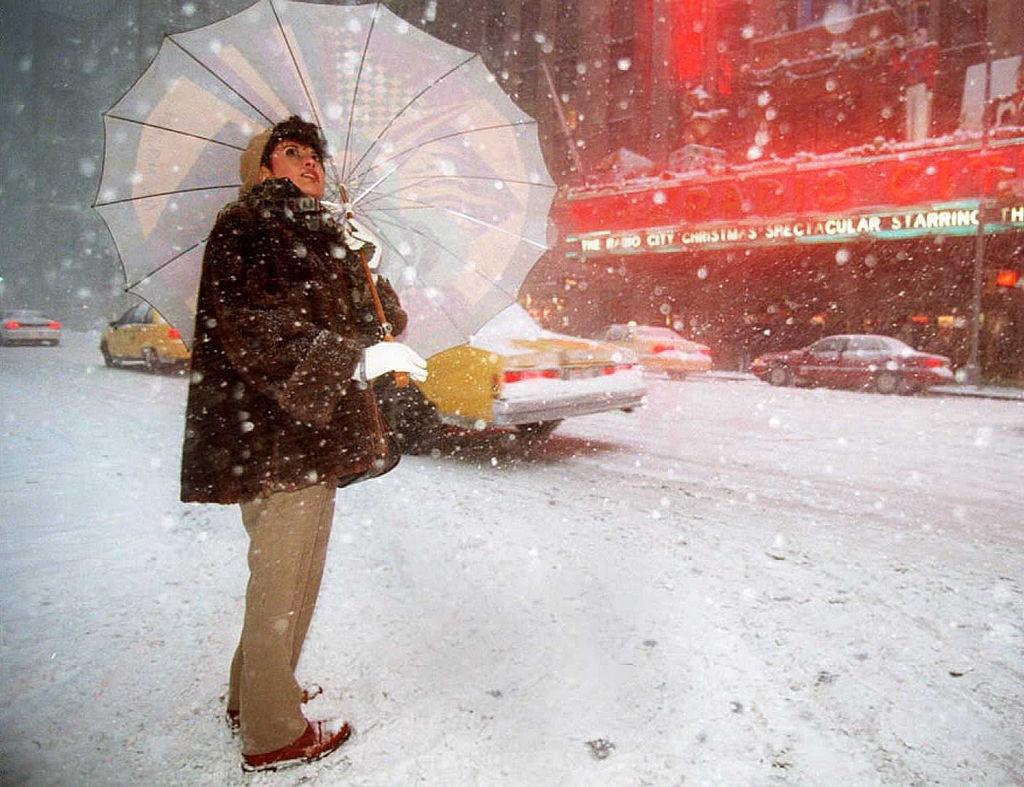 A woman looks skyward as she waits to cross the street outside Radio City Music Hall during the heavy snowfall 07 January in New York.