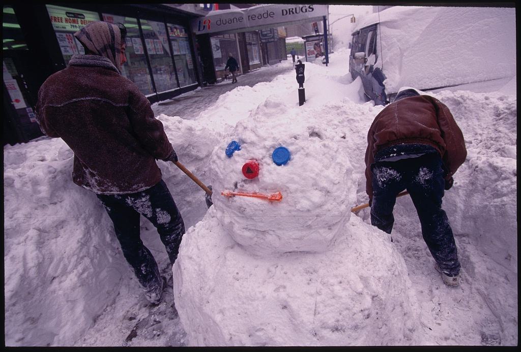Two Men Shovel Snow Around a Snowman