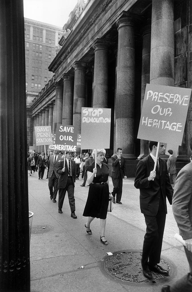 Protesters marching with placards outside Penn Station to save the building from demolition, New York City. Their signs read 'Preserve Our Heritage' and 'Stop Demolition.