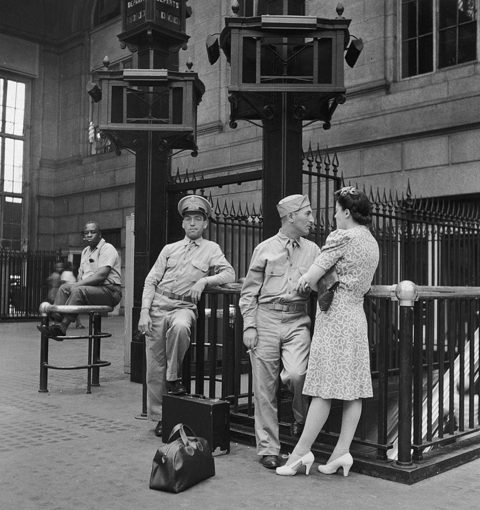 Soldiers smoke and stand with a young woman while waiting in the Pennsylvania railroad station, New York City, 1942