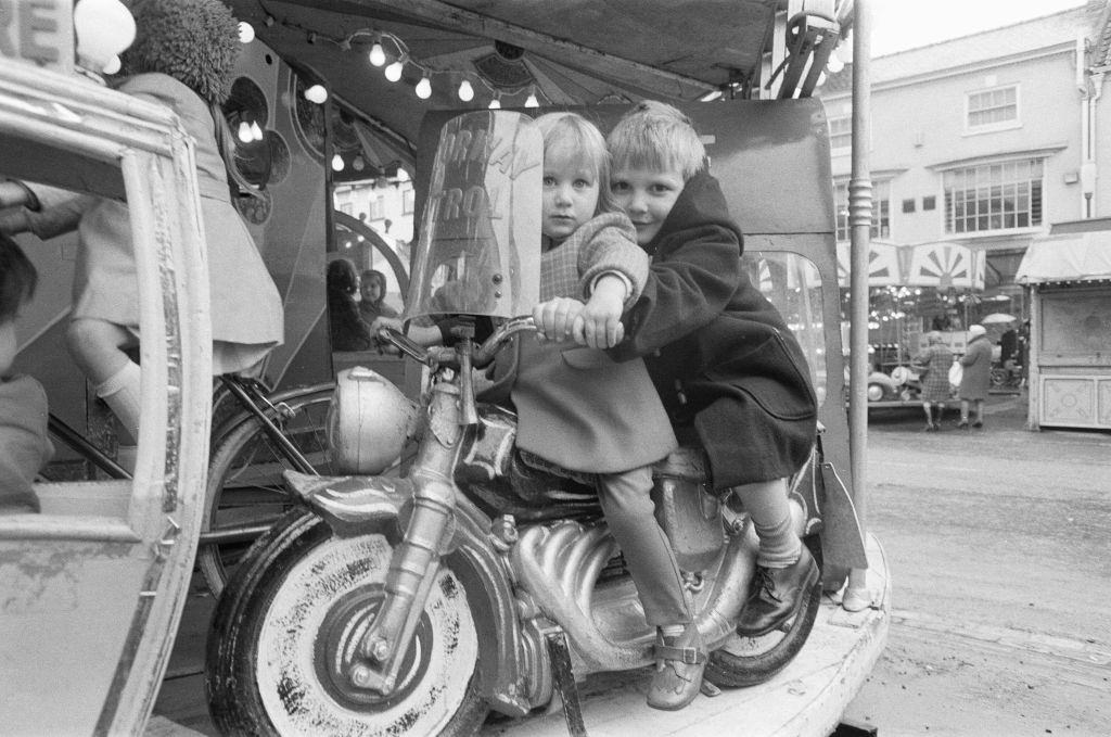 Brother and sister riding a motorcycle on a child's roundabout at the Northallerton May Fair 1971.