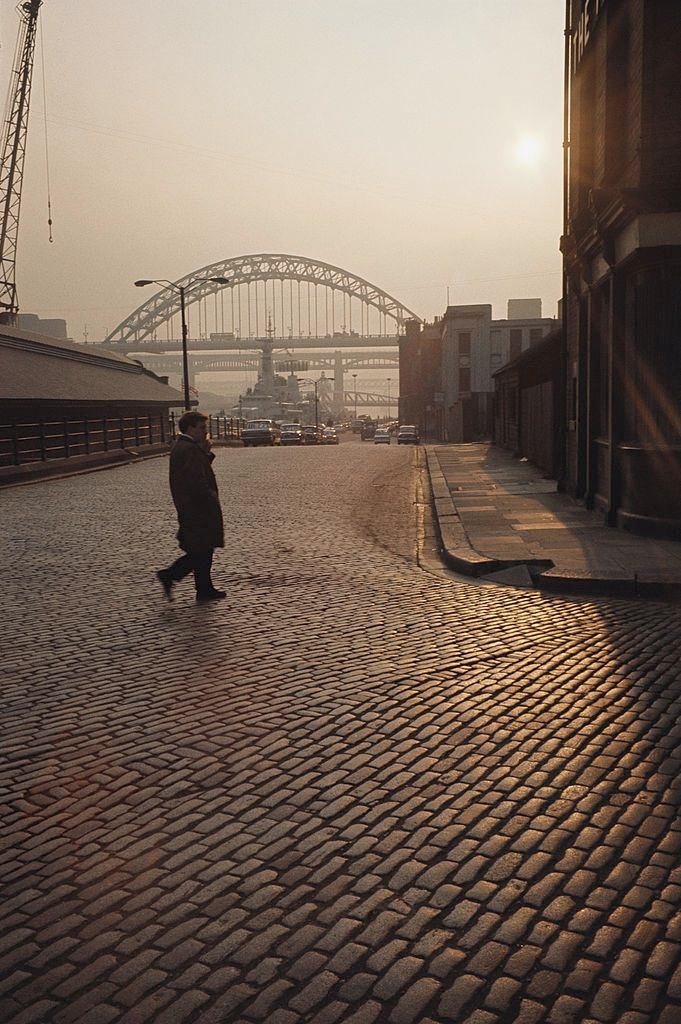 A lone man walks across the cobbled street in view of the Tyne bridge, Newcastle, 1970.