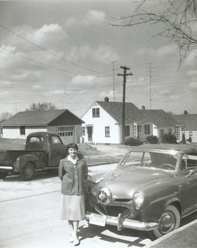 A young lady posing with a 1950 Studebaker Champion Convertible in a suburban street.