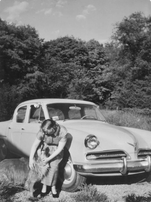 A blonde lady cuddling with a dog in front of a 1953 Studebaker Commander DeLuxe Sedan, 1954