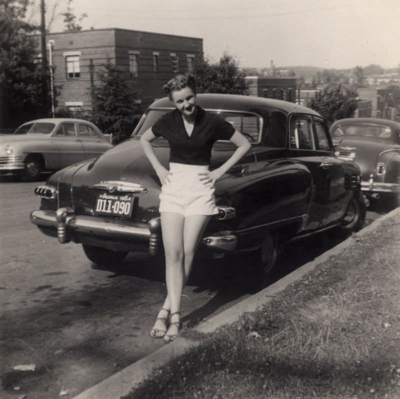 A pretty girl posing with a 1947 Studebaker Commander Regal DeLuxe in a city street in summertime.