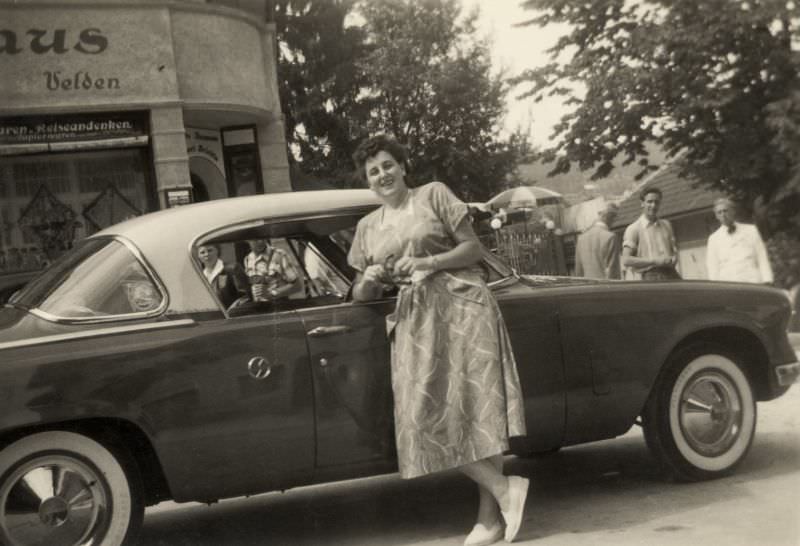A cheerful middle-aged lady posing with a 1953 Studebaker Champion Regal Starliner in summertime, 1955