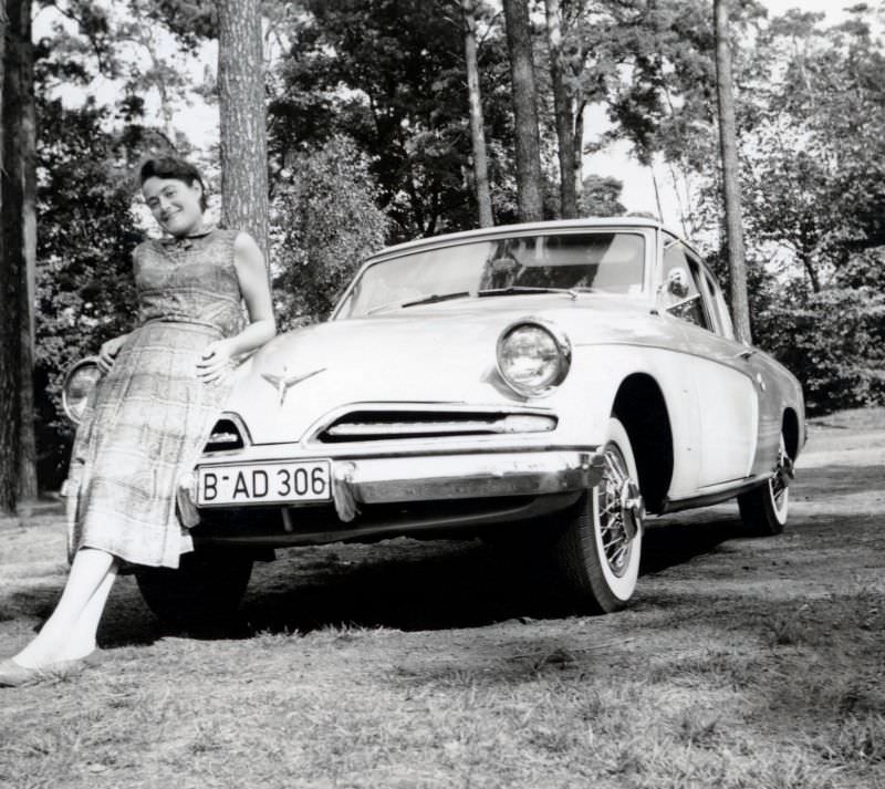 A cheerful young lady posing with a 1953 Studebaker Champion de Luxe Starlight Coupe in summertime, 1951
