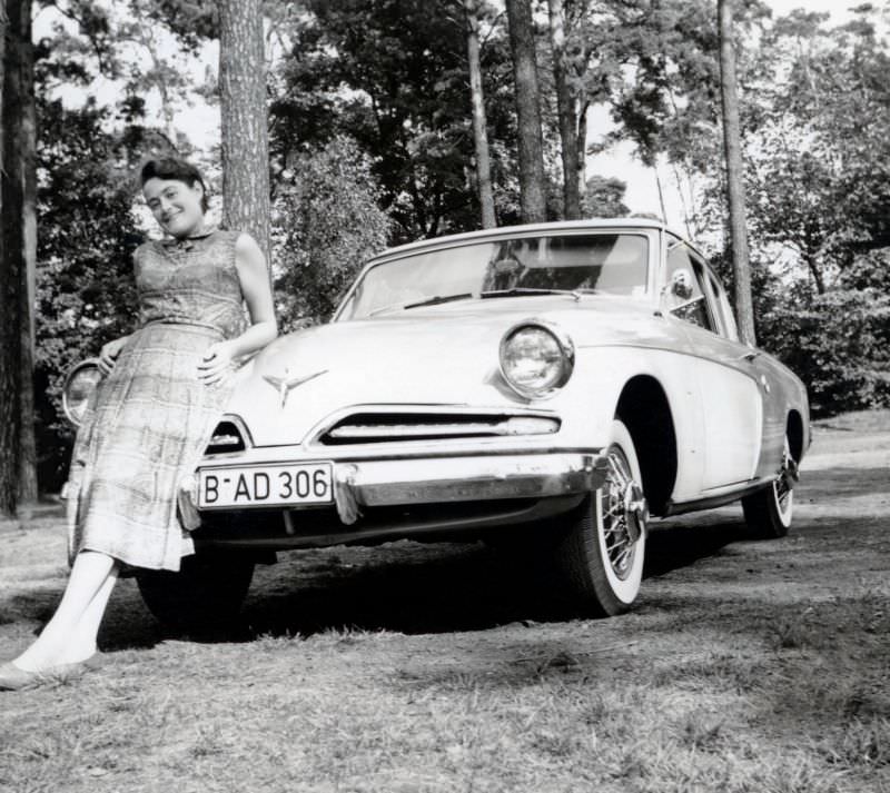 A cheerful young lady posing with a 1953 Studebaker Champion de Luxe Starlight Coupe in summertime, 1951