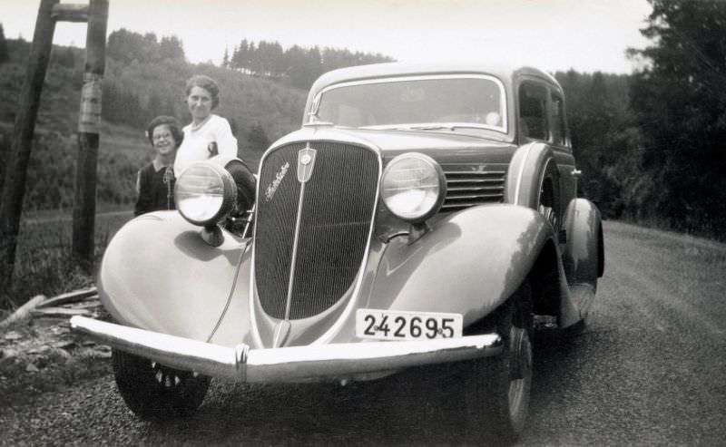 A mother and her daughter posing with a 1934 Studebaker Land Cruiser on a gravel road in the countryside.