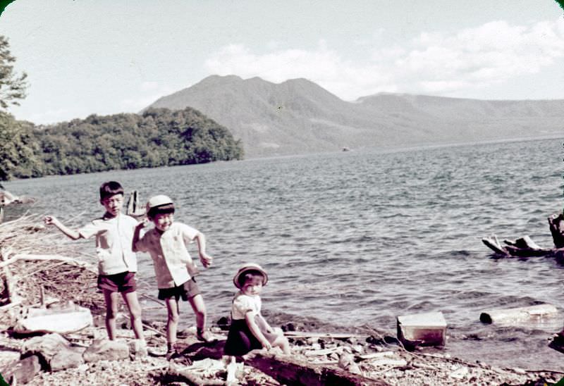 Two boys throwing rocks and a girl looking at the camera on a shore in Japan