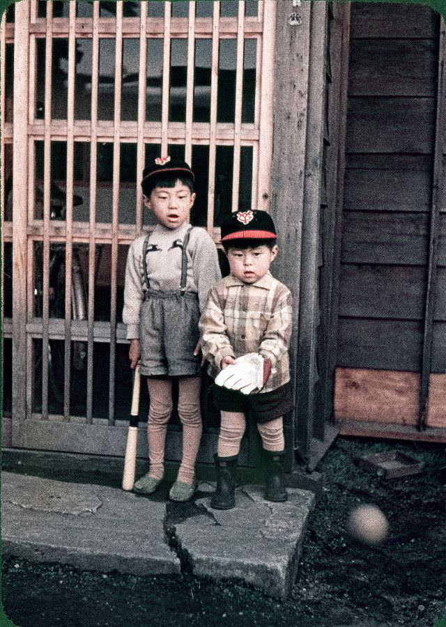Two Japanese kids (one with a baseball glove, one with a bat) wearing Yomiuri Giants caps