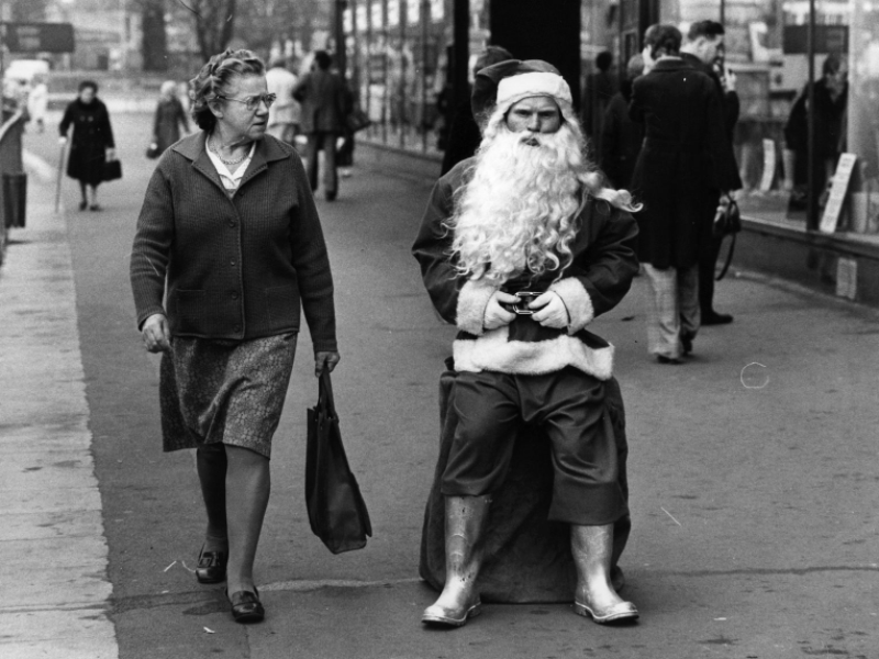 A woman glance at a surly looking Santa in a busy shopping street, 1975.