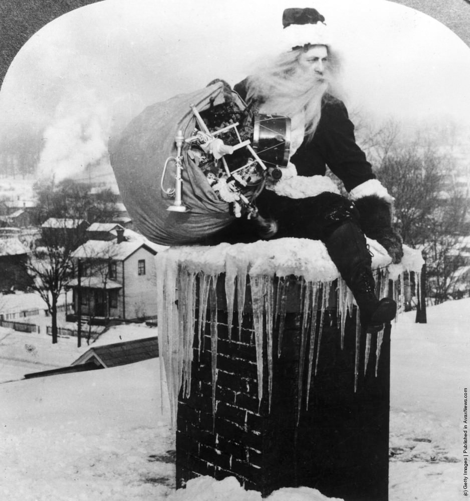 Santa Claus brings a sack full of toys down a chimney on a snowy rooftop, 1925