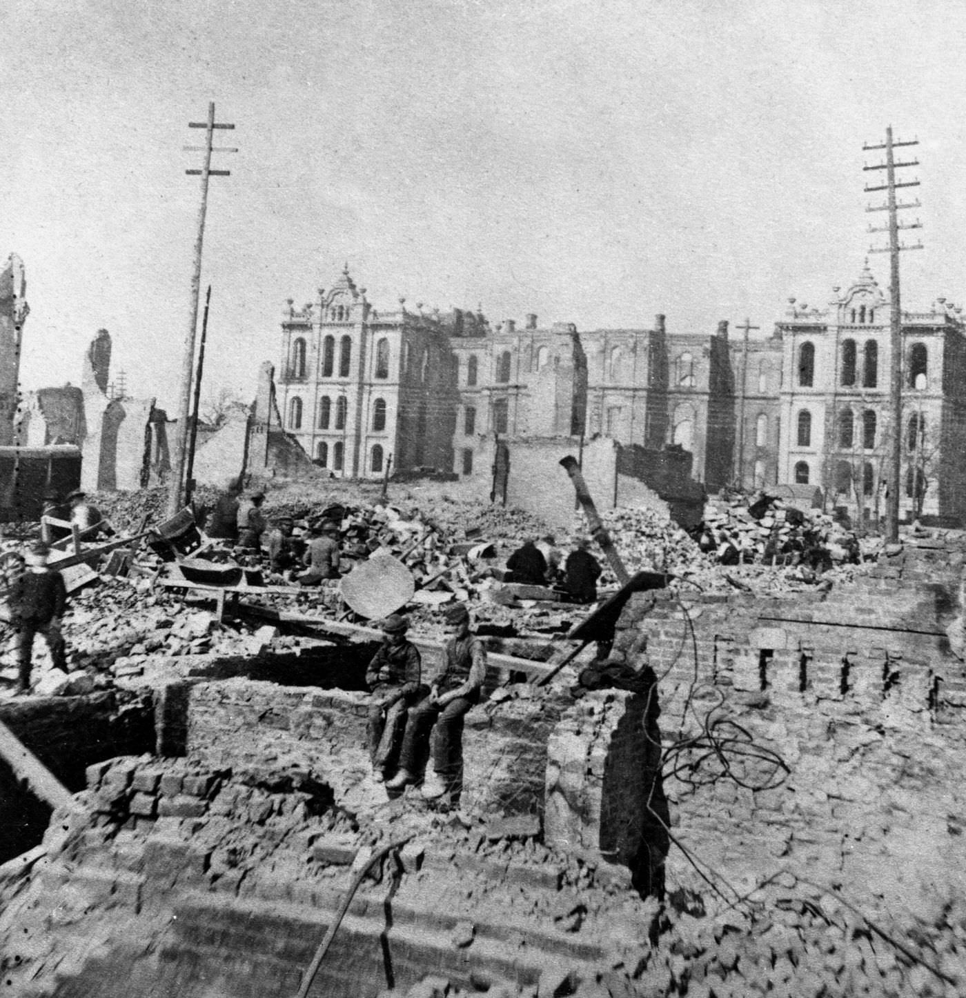Two boys sit on top of a partial stone wall in the wreckage of a burned-out building at Madison and Clark Streets, with the Court House in the background following the fire.